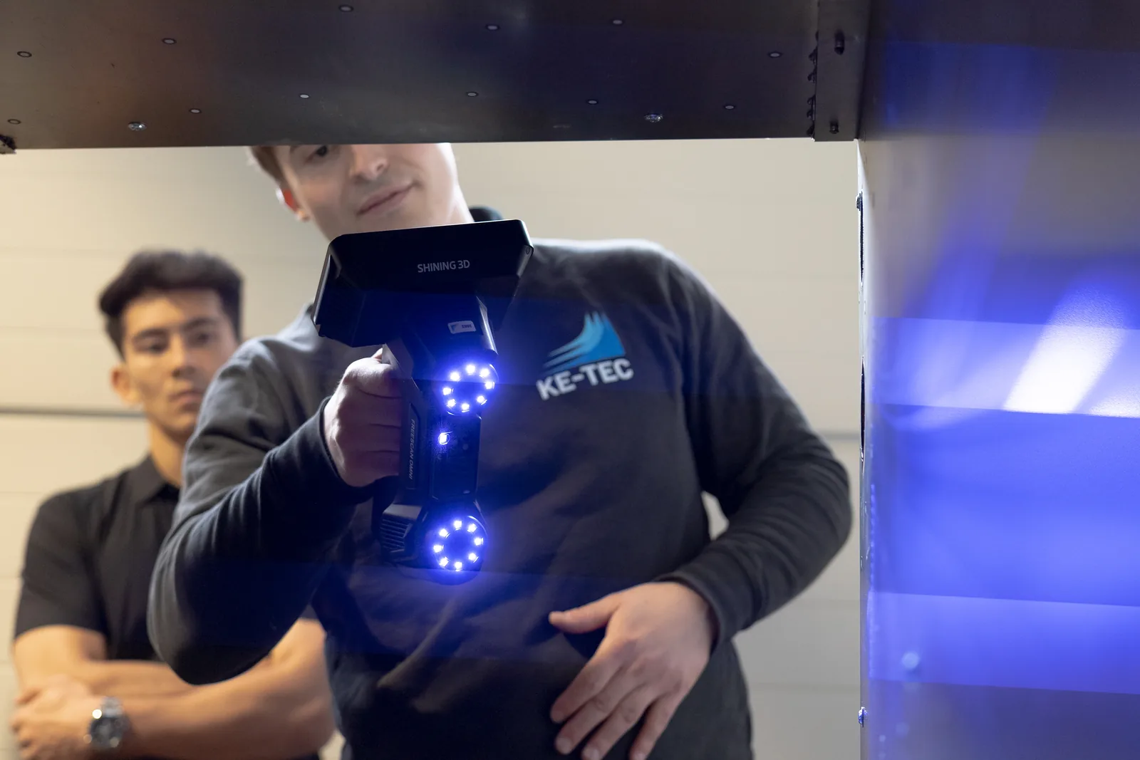 Technician scanning a large dark panel with the FreeScan Omni Lite, blue laser projection visible on the surface